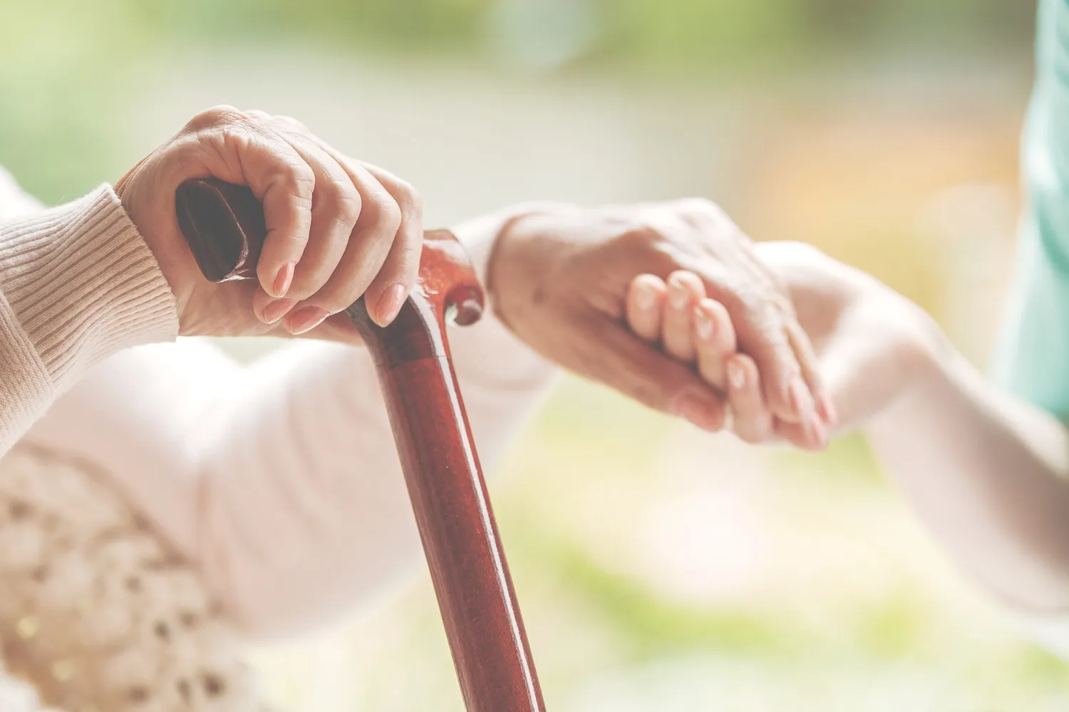 Nahaufnahme einer älteren Dame, die in der einen Hand einen Gehstock und in der anderen die Hand der Krankenschwester hält