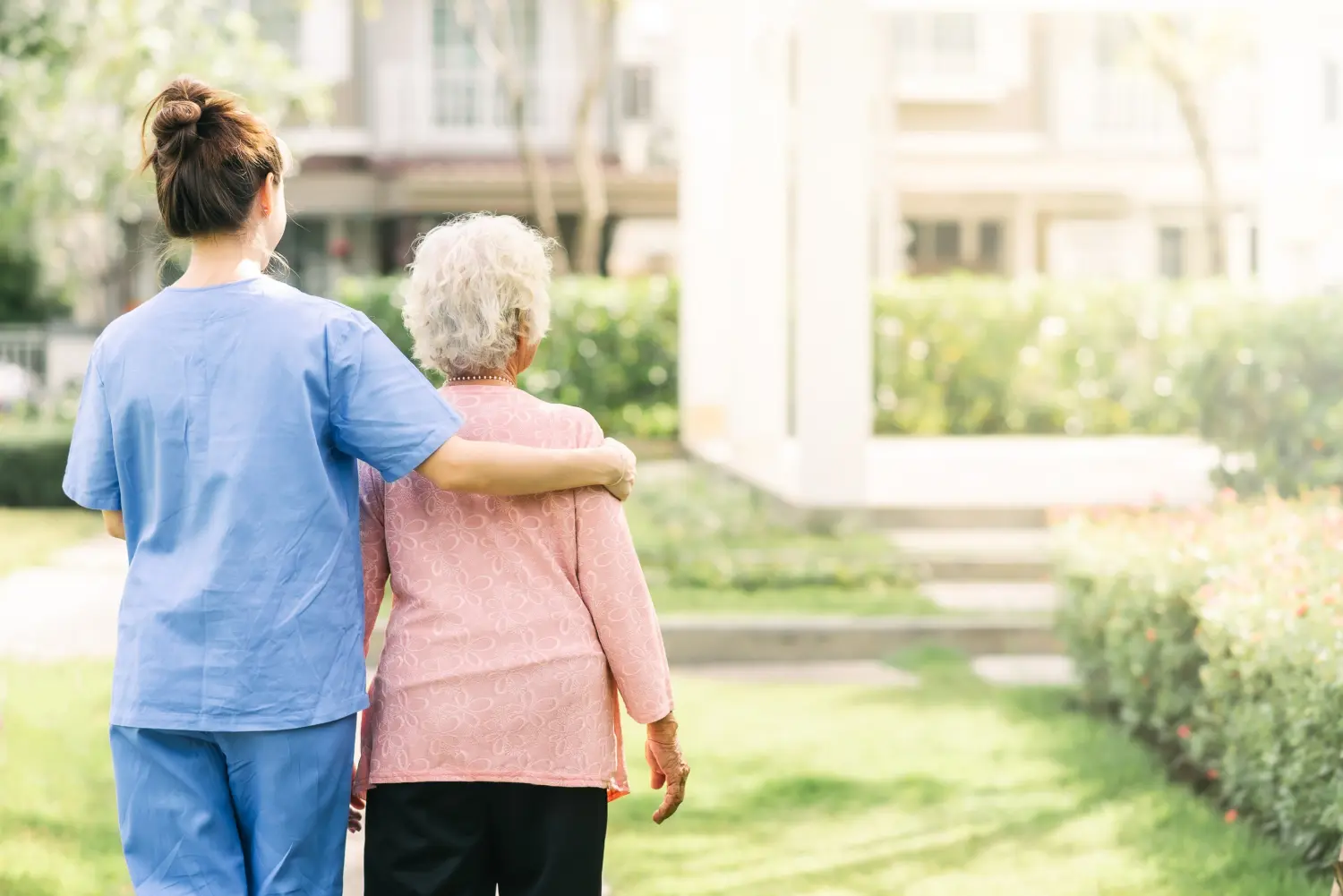 Krankenschwester-Betreuer unterstützt das Gehen mit einer älteren Frau im Freien